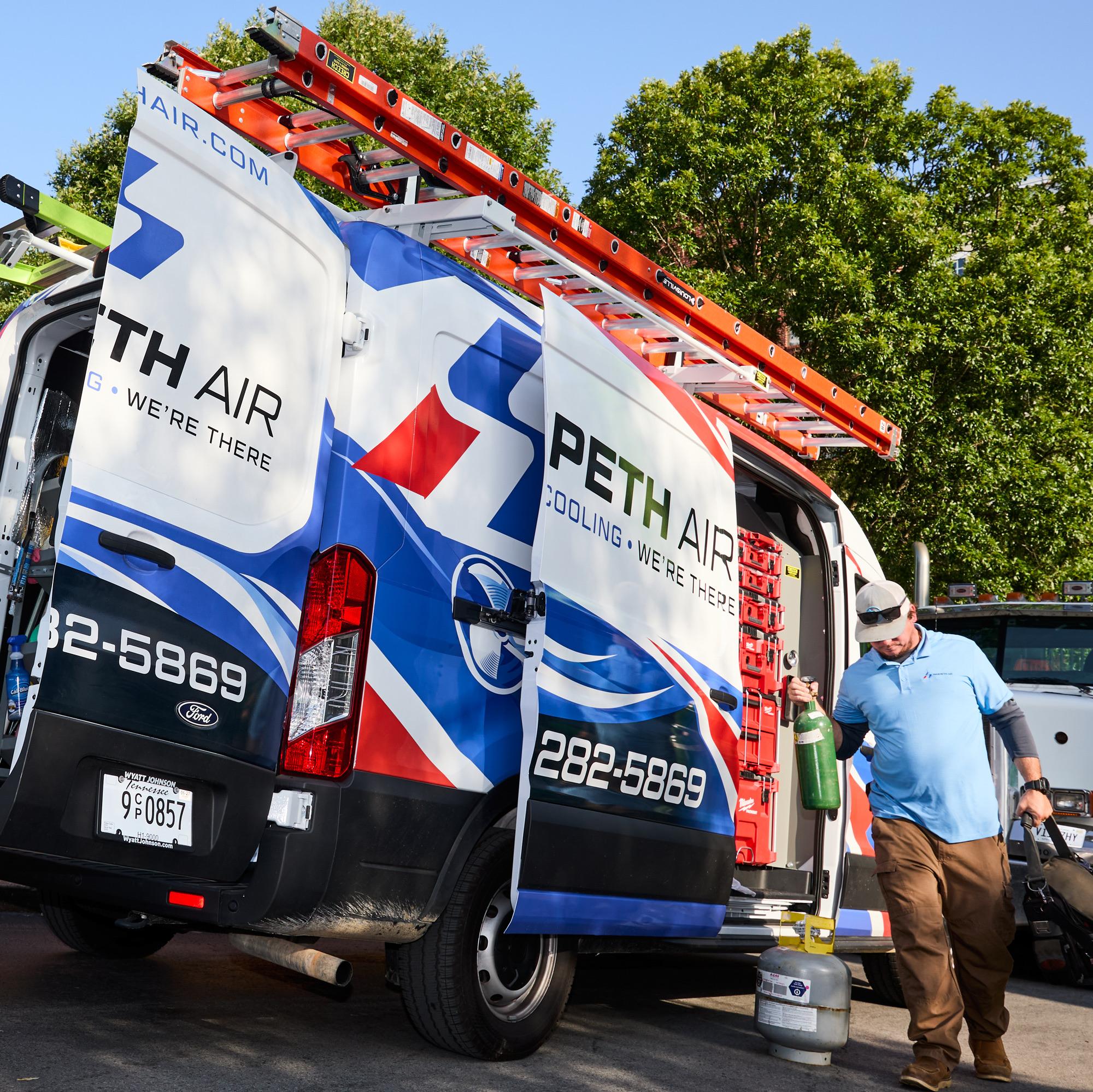 Harpeth Air technician carrying tools and a cylinder beside an open service van